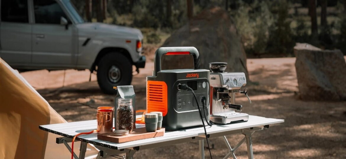 Jackery Explorer alimentant une machine à espresso sur une table de camping, près d'un 4x4 et d'une tente dans une forêt de pins