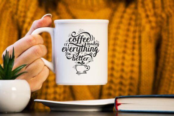Gros plan d'une personne tenant un mug blanc avec l'inscription "Coffee makes everything better."
