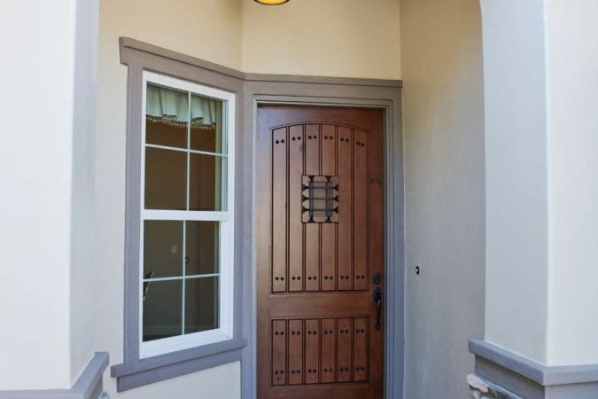 Porte d'entrée en bois massif avec ferronnerie noire sur facade grise, exemple d'une entrée reste toujours rangée grâce à un espace épuré et bien délimité.