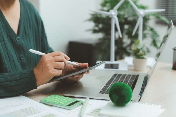 Une personne travaillant sur une tablette avec des éoliennes miniatures et un globe vert sur son bureau, symbole de la planification du tourisme responsable.