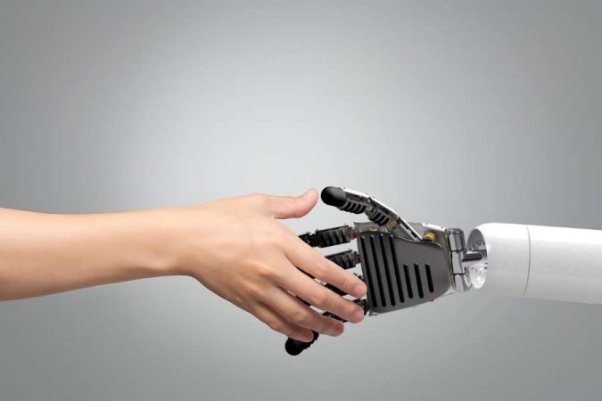 Une main humaine s'apprête à serrer une main robotique articulée sur un fond gris épuré.