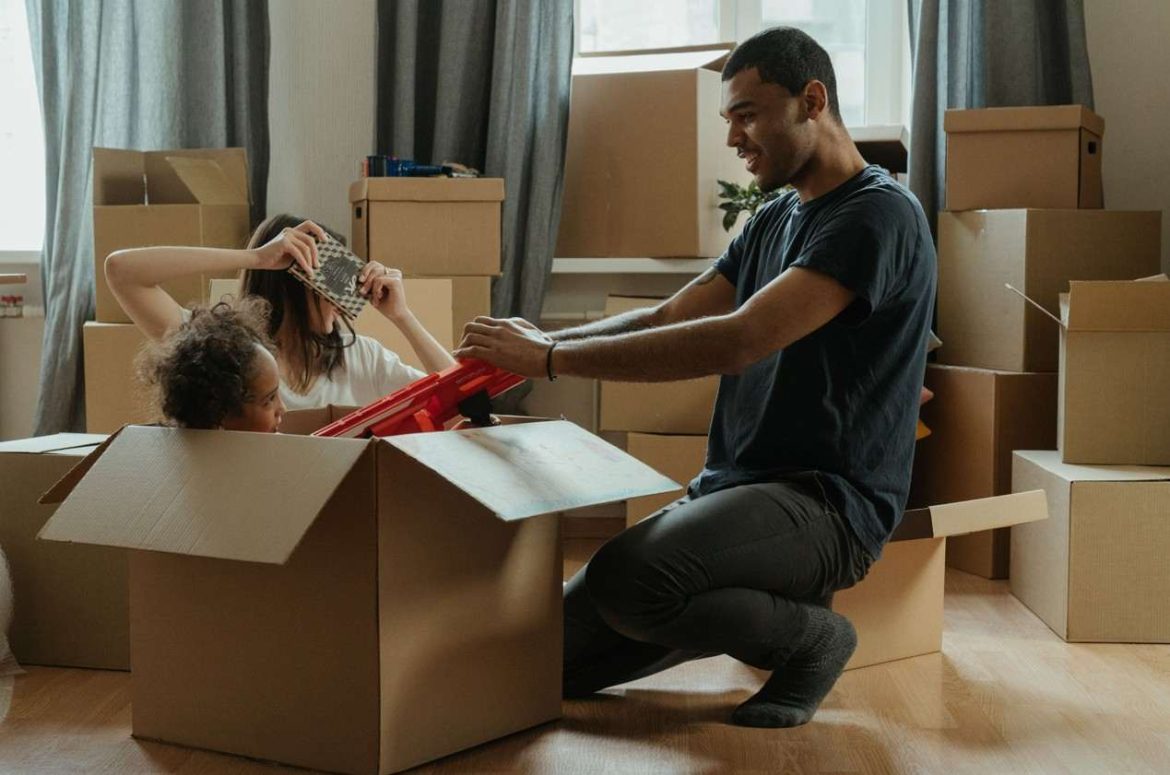Un père souriant aide son jeune enfant installé dans un grand carton de déménagement, illustrant nos astuces pour déménager sereinement avec des enfants en bas âge.
