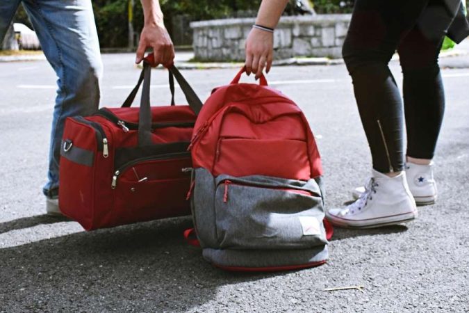 Deux personnes tiennent un sac de voyage et un sac à dos rouge lors d'un départ.